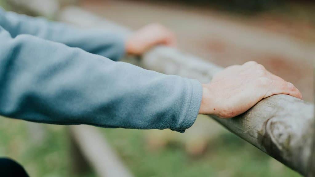 A close-up of hands resting on a wooden fence.