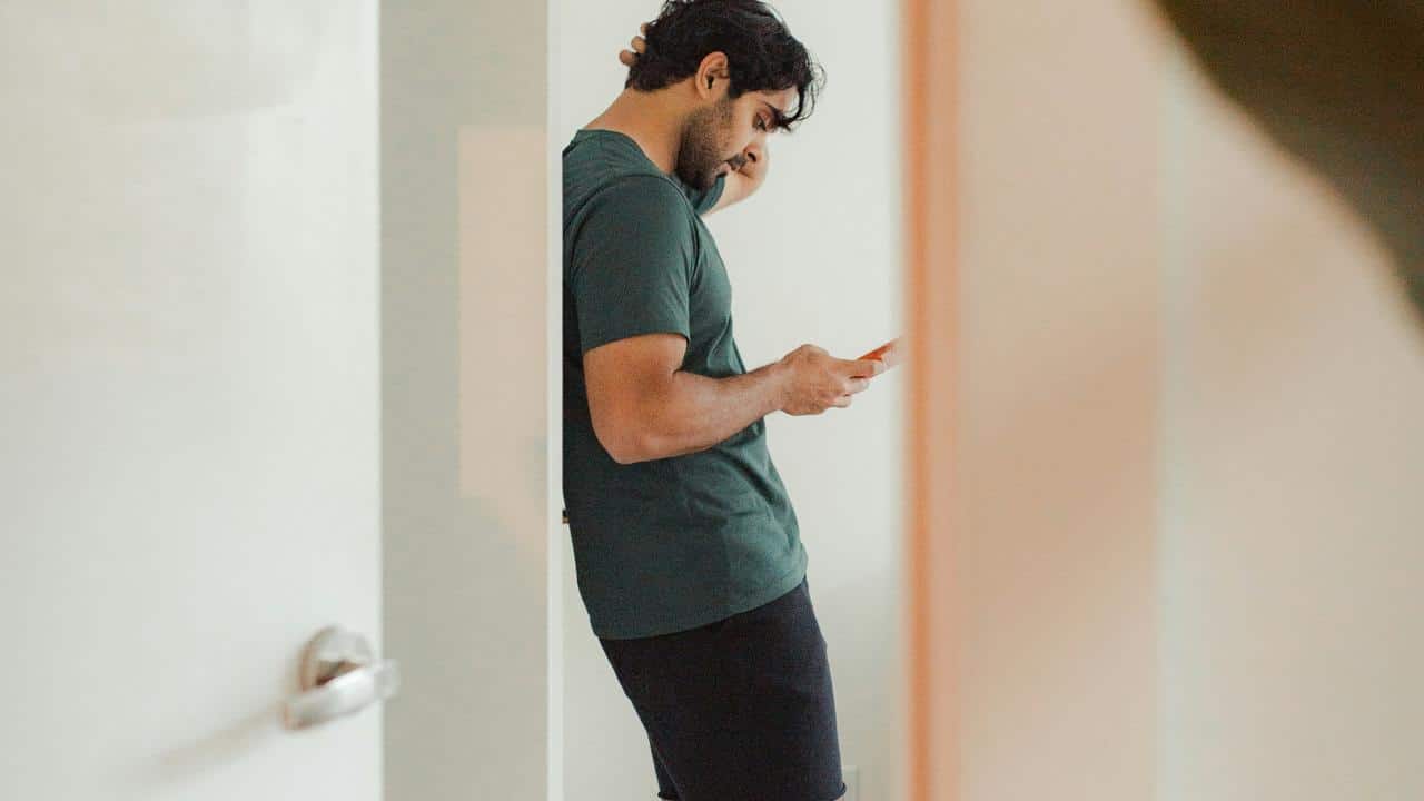 A man leaning against a wall while looking at his phone.