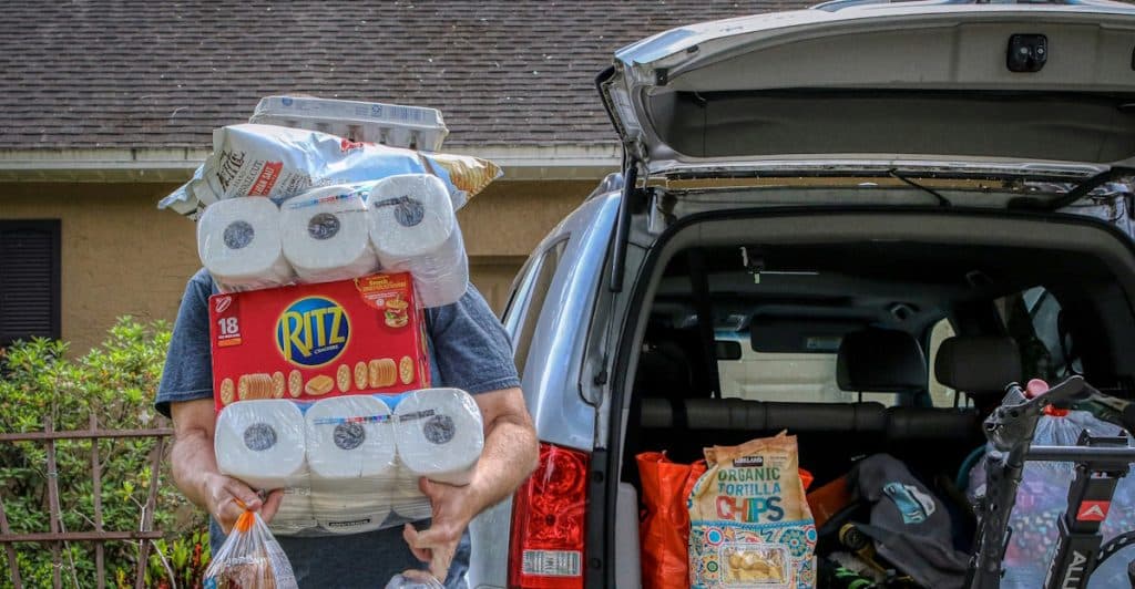 A person carries multiple grocery items while unloading a car.