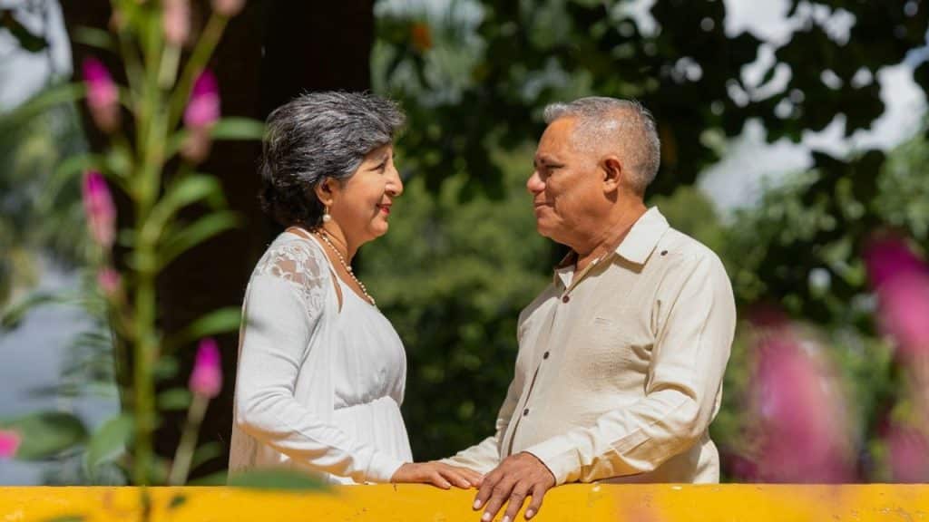 Elderly couple in white clothes facing each other and holding hands in a park.