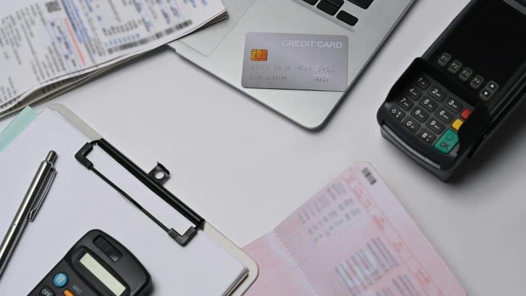 A credit card rests on a laptop near a terminal, bills, and a calculator.
