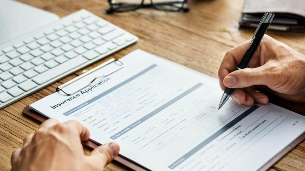 Hands are shown filling out an Insurance Application form next to a keyboard.