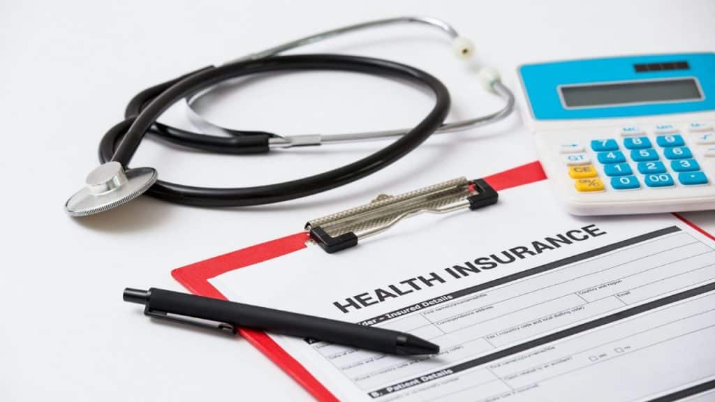 A stethoscope, calculator, and pen are arranged on a Health Insurance form.