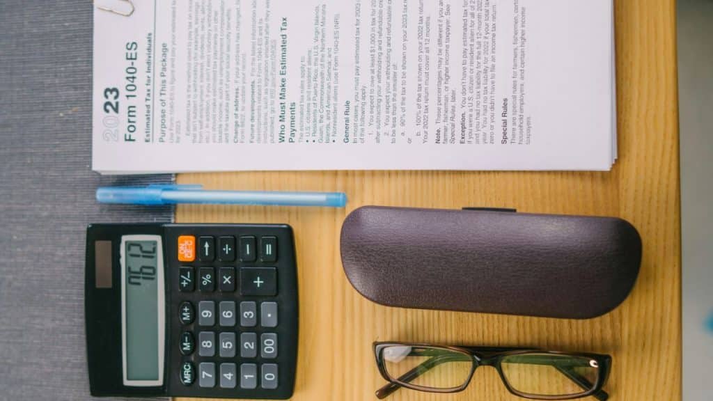 A calculator, pen, eyeglasses, and tax form 1040-ES are on a wooden table.