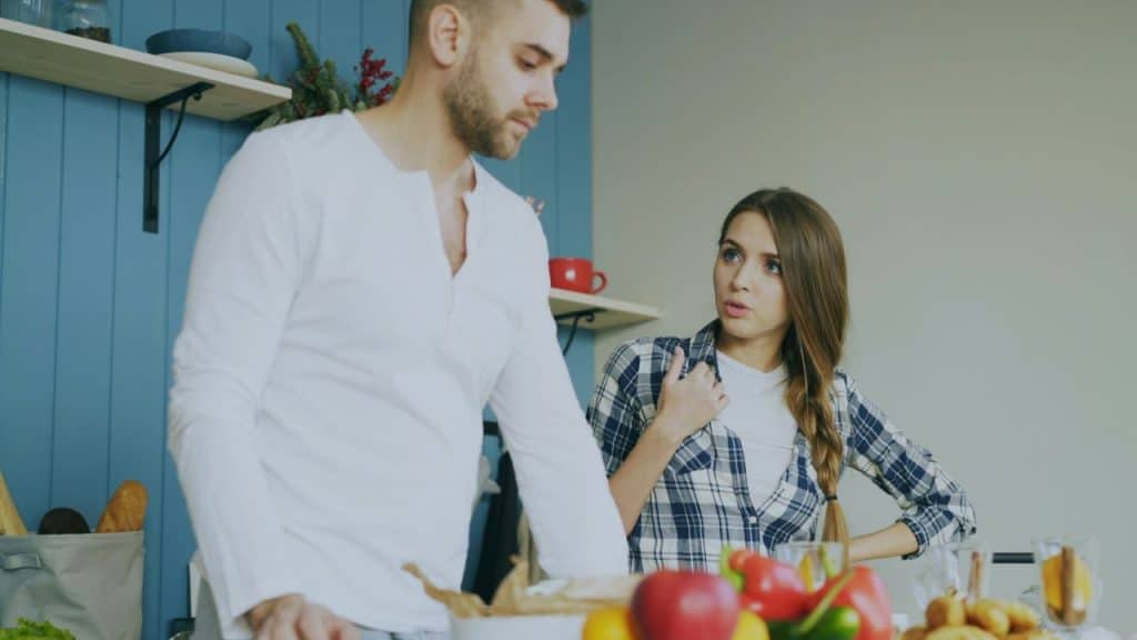 A concerned woman with a braid confronts a serious man in a kitchen.