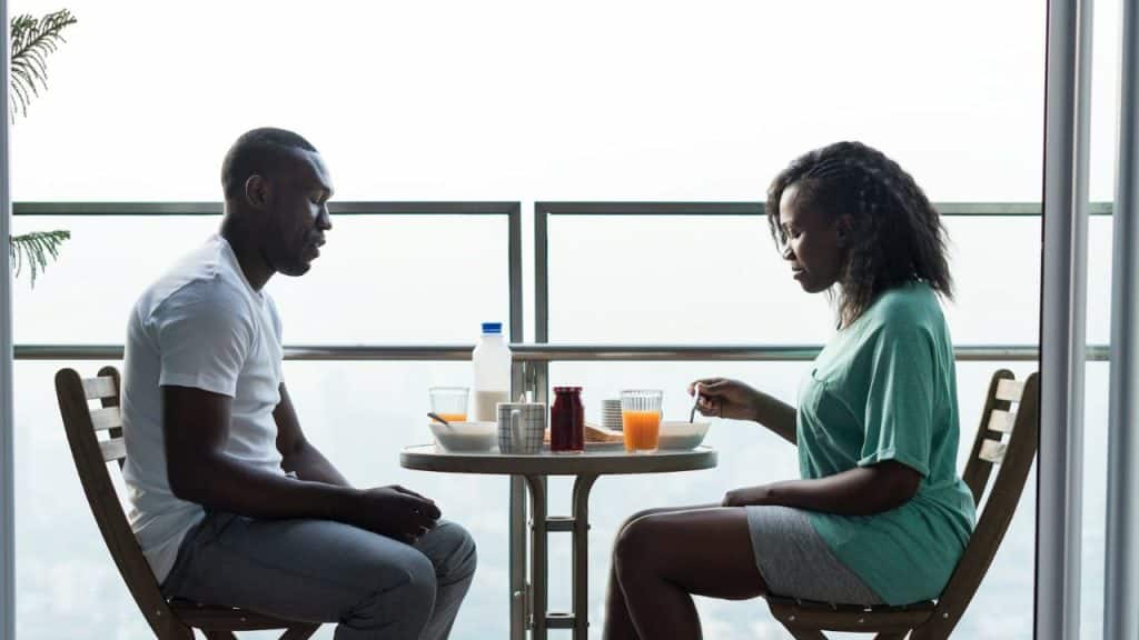 A Black couple having a quiet breakfast on a balcony with a moody sky.