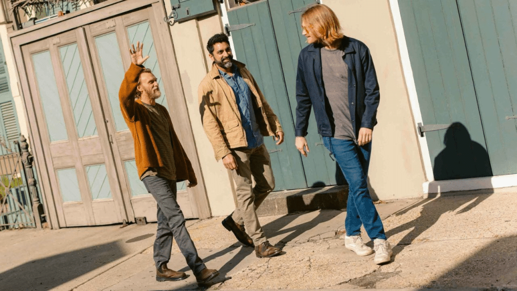 Three diverse men are laughing and walking down a sunny, historical street.