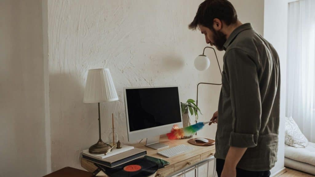 Man dusting a desktop computer and keyboard with a rainbow duster on a wooden desk.