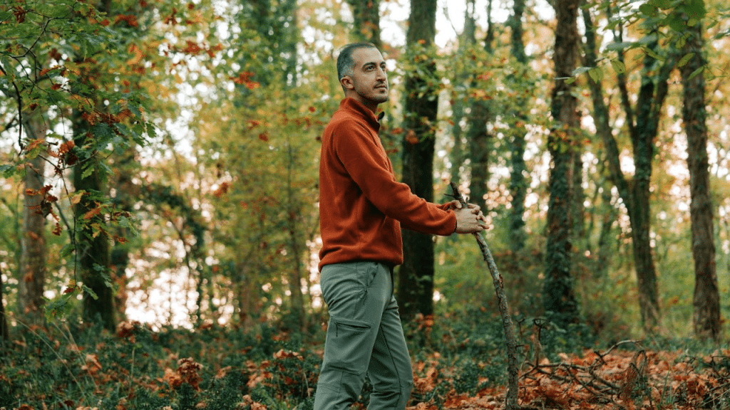 A thoughtful man with a walking stick stands alone in an autumnal forest.
