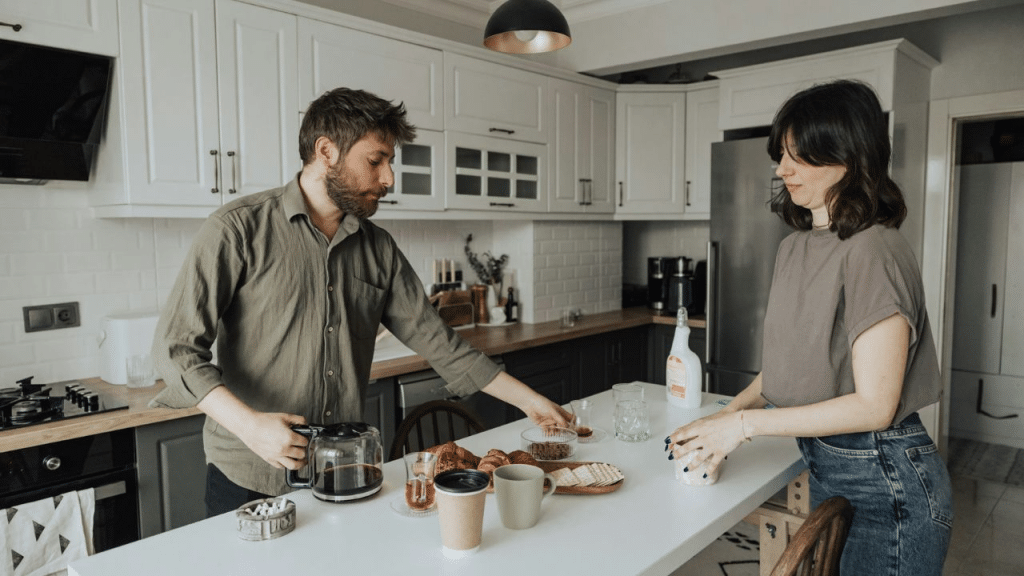 A serious man and woman prepare breakfast in a white and modern kitchen.