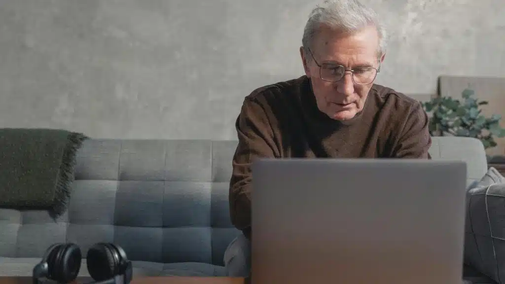 A senior man sitting on a couch and using a laptop.