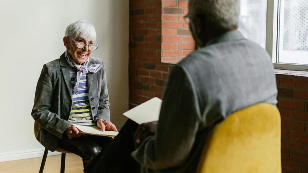 A senior woman smiling while talking to a man during a meeting.