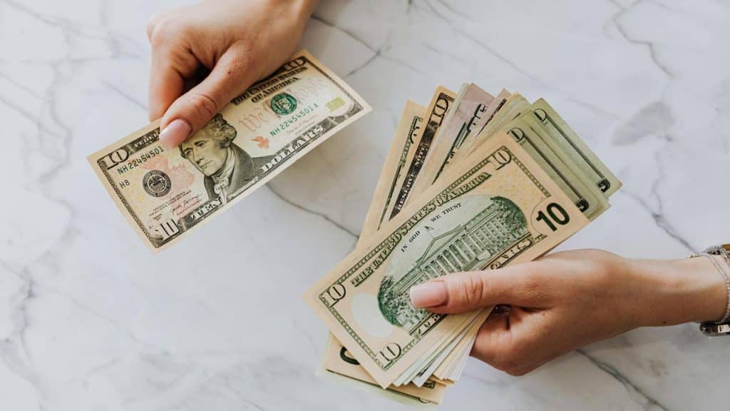 A person holding and counting a stack of US dollar bills.