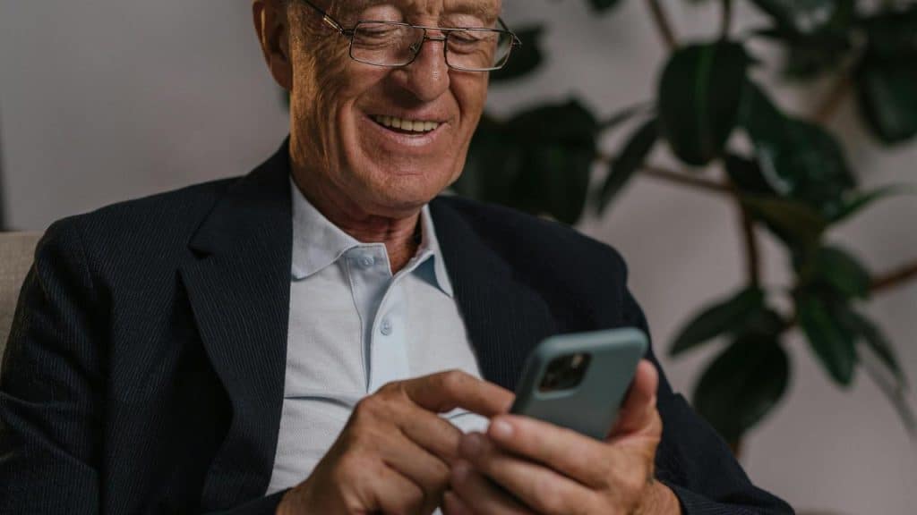 A senior man smiling while using a smartphone.