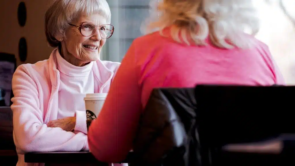 An elderly woman smiling while chatting with a friend at a café.
