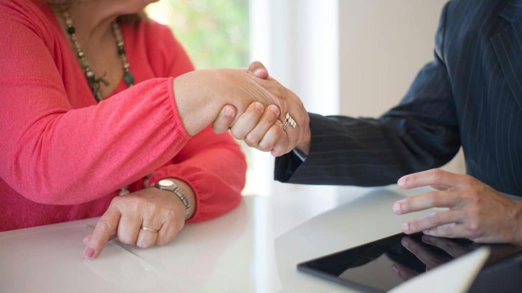 An older woman shaking hands with a man across a desk.