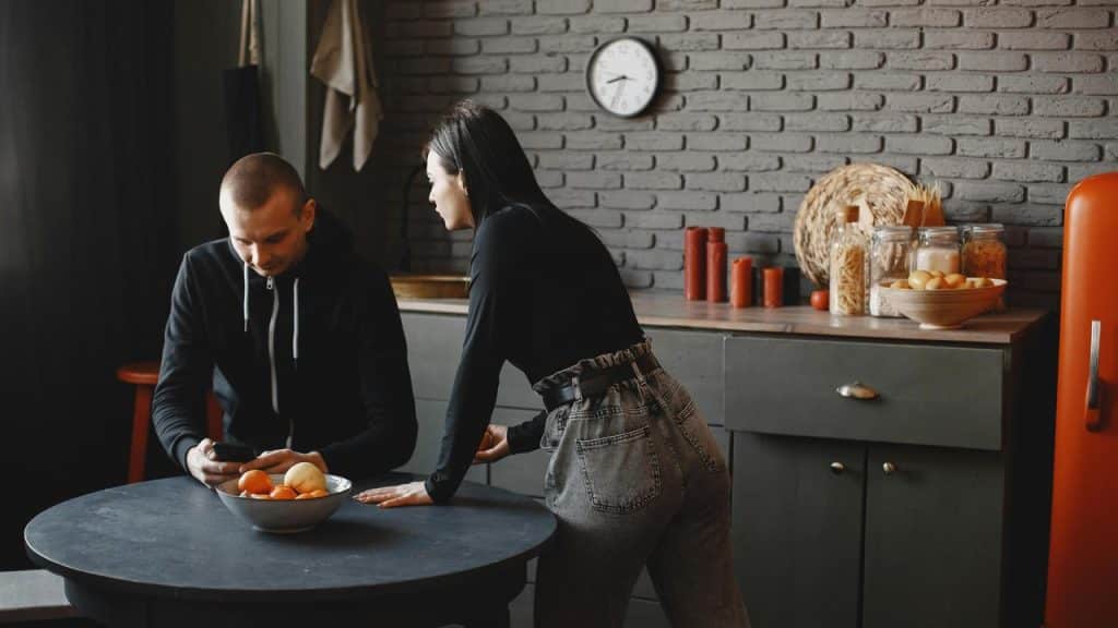 A woman leaning on a table while talking to a man looking at his phone.
