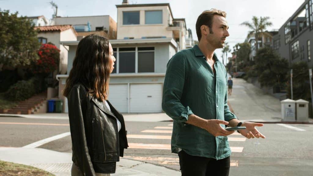 A man gesturing while talking to a woman on a street corner.