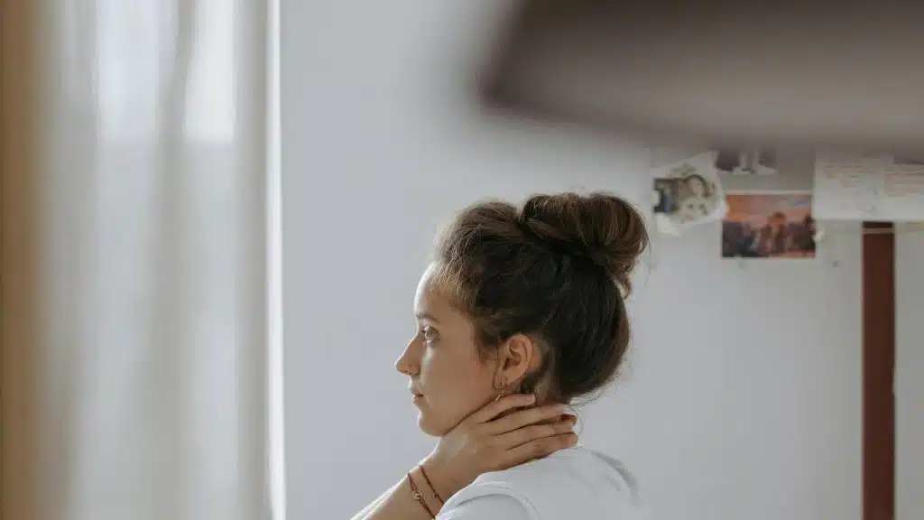 A woman sitting with her hand on her neck looking to the side.