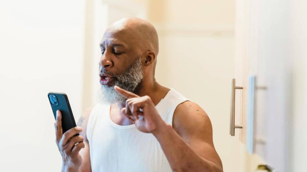 A man holding a smartphone and speaking with a raised finger.
