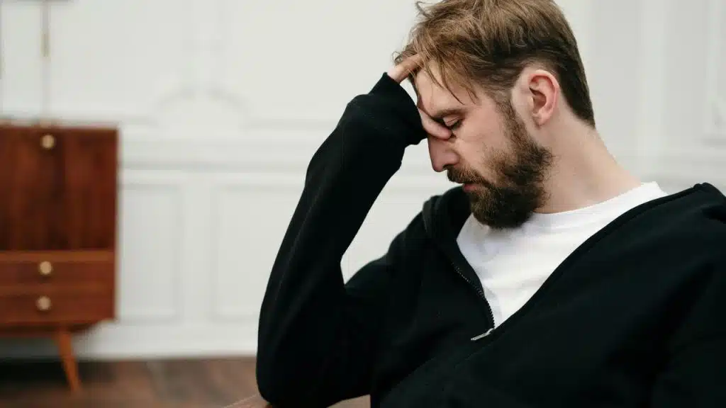 A man sitting with his hand on his forehead looking down.