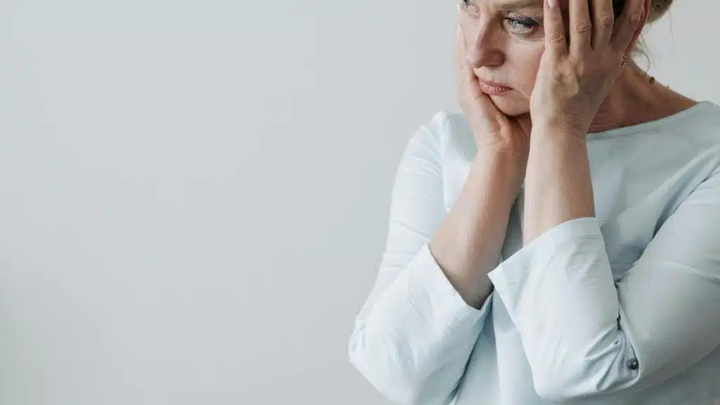A woman sitting with her hands on her face looking upset beside an open photo album.