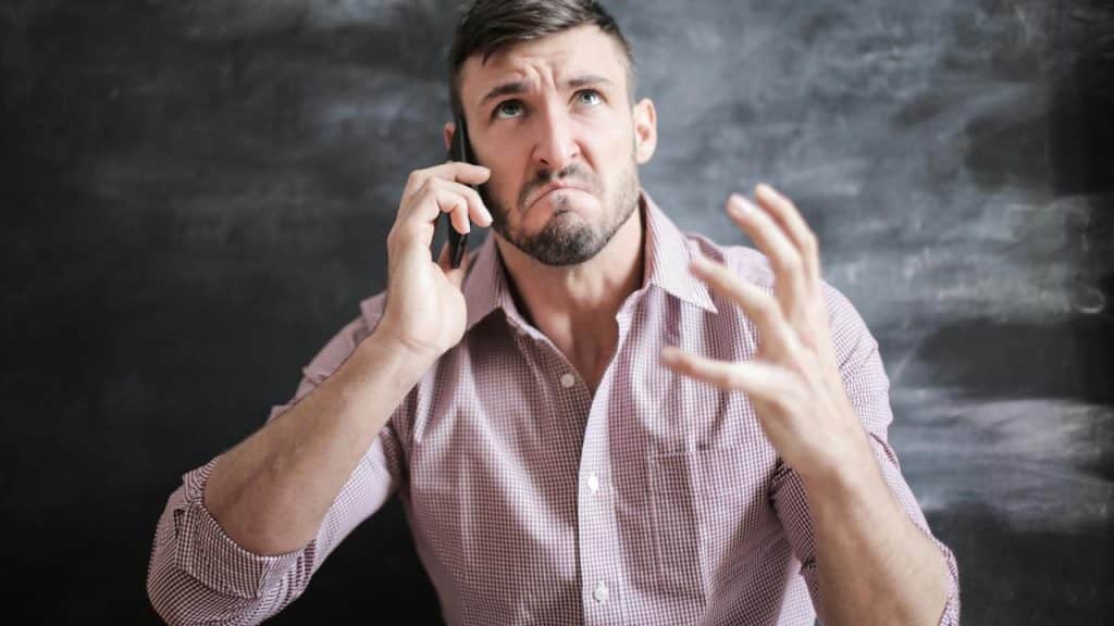 A man talking on the phone with a frustrated expression and raised hand.