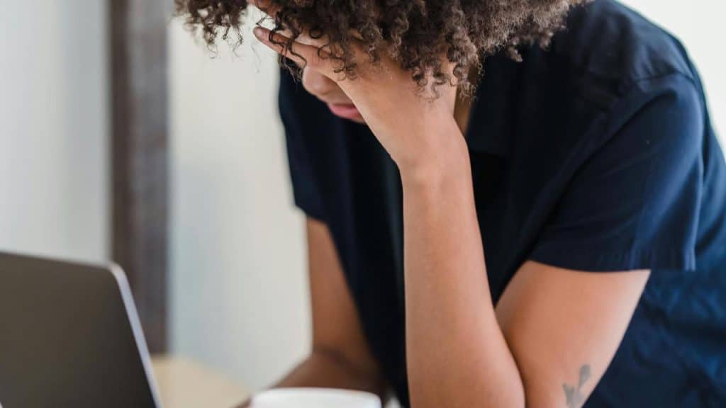 A woman sitting at a desk with her head resting on her hand looking stressed.