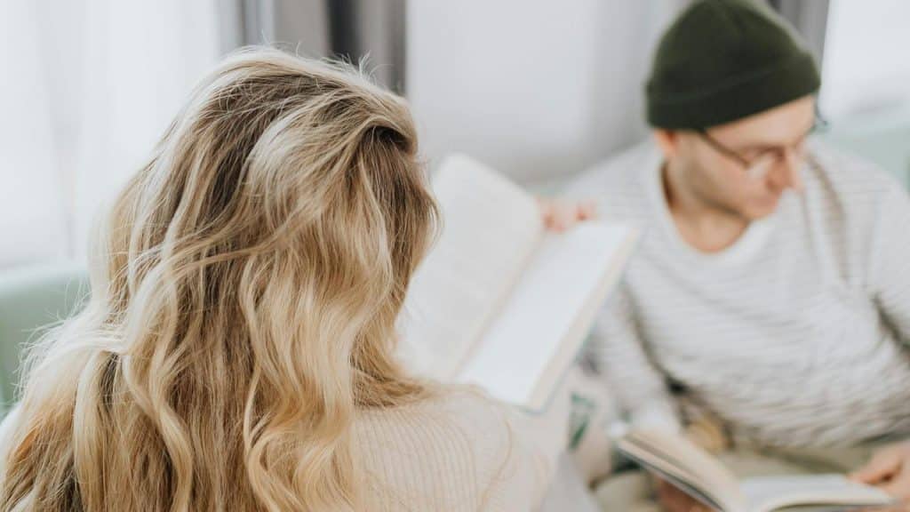 A woman holding a book while sitting near a man who is also reading.