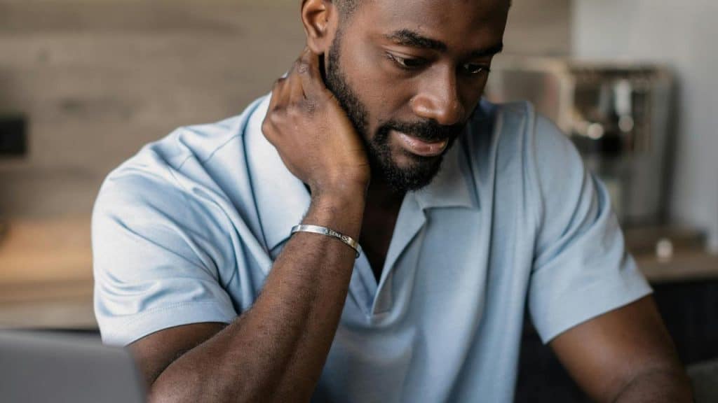 A man sitting at a table resting his hand on his neck while looking down.