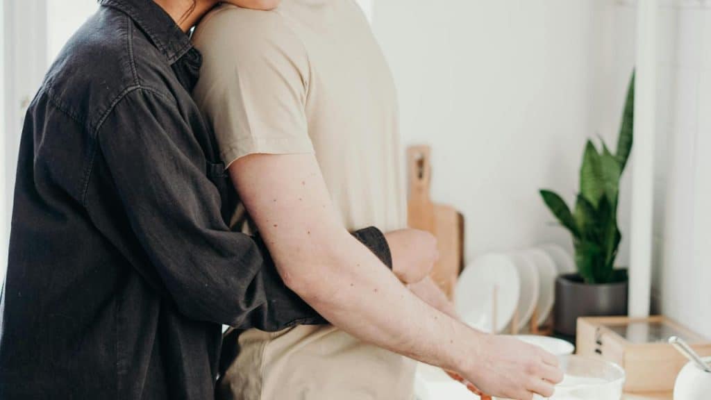 A person hugging someone from behind while they prepare food in the kitchen.