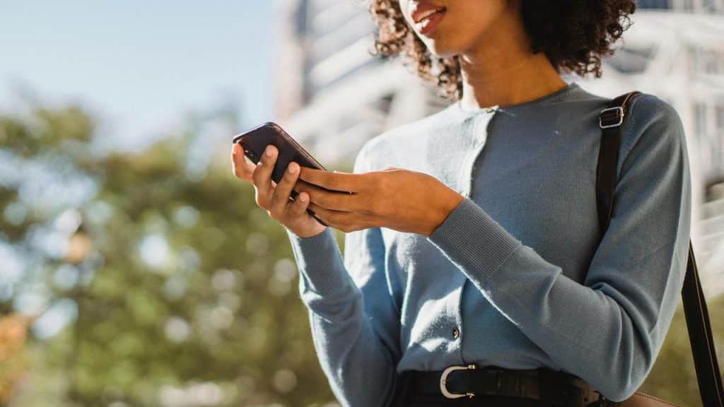 A woman standing outdoors holding a smartphone with both hands.