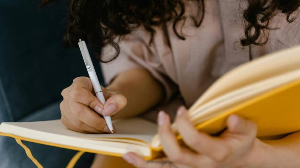 A person writing in a yellow notebook.