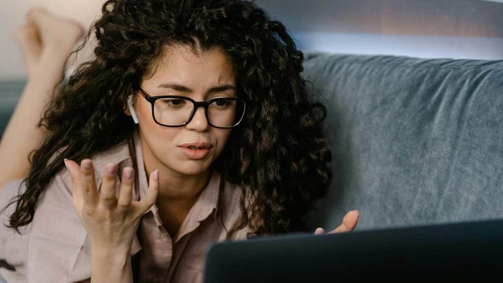 A woman wearing glasses using a laptop and gesturing with her hand.