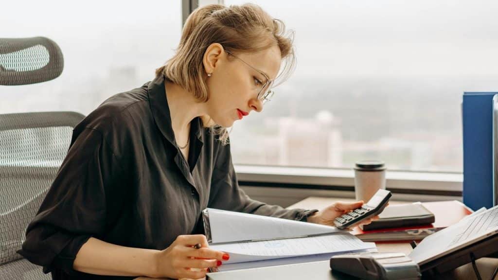 A woman working at a desk using a calculator and reviewing documents.