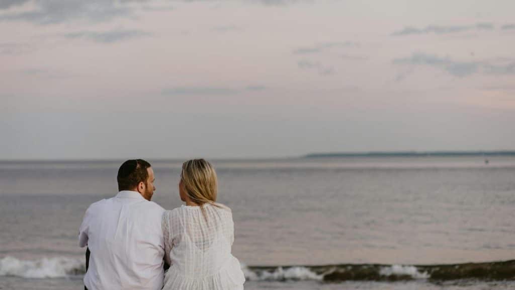 A couple sitting by the beach facing the ocean.
