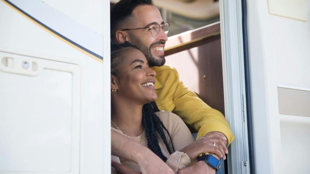 A smiling couple standing at the doorway of a camper van.