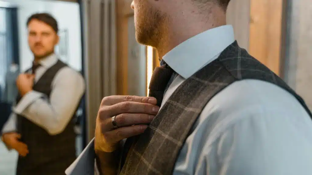 A man adjusting his tie while looking at himself in the mirror.