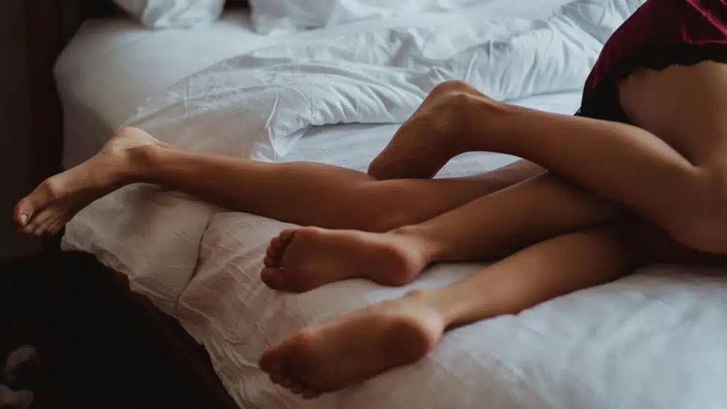 A couple lying together on a bed with their legs intertwined.