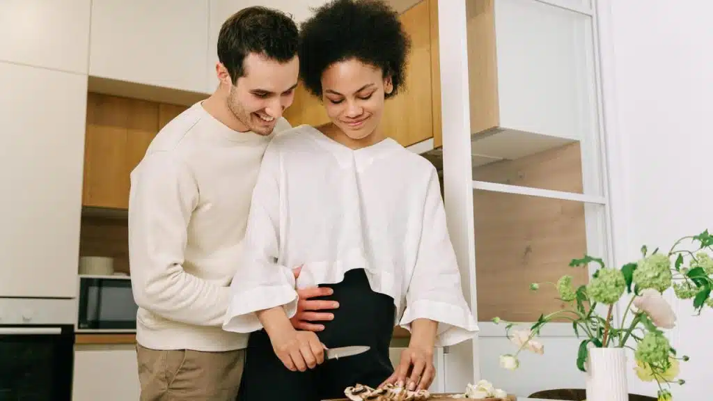 A couple standing together in a kitchen while preparing food.