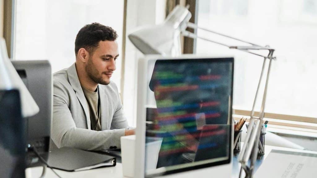 A man in a gray blazer working at a computer in an office.