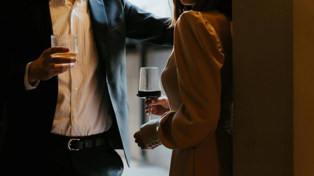 A man in a suit and a woman in a dress holding drinks at a dimly lit bar.