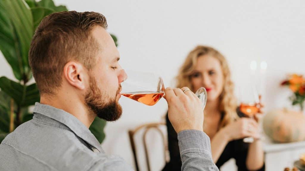 A man sipping wine while a woman smiles at him across the table.