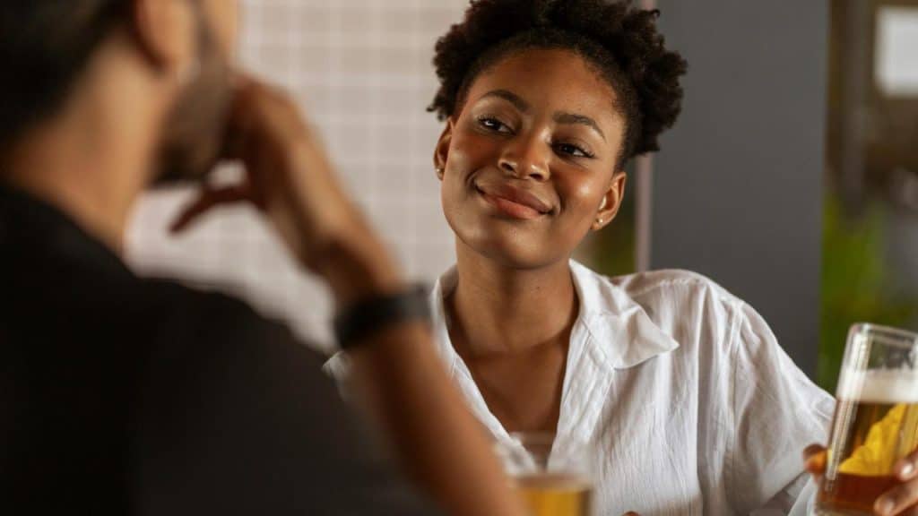A woman smiling at a man while holding a glass of beer.