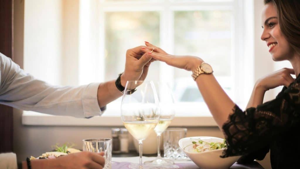 A man holding a woman’s hand across a restaurant table with wine glasses.
