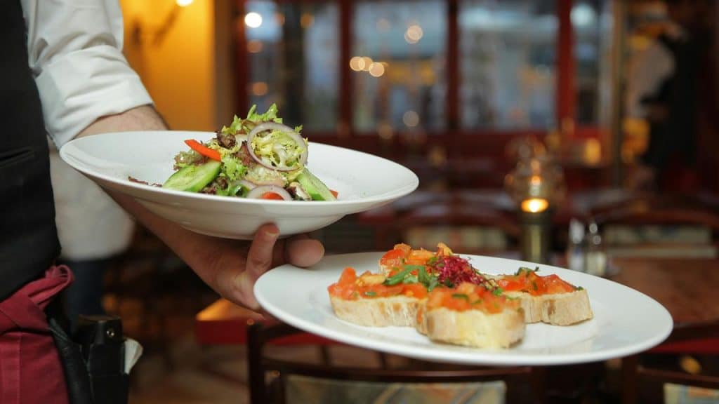 A waiter carrying plates of salad and bruschetta in a restaurant.