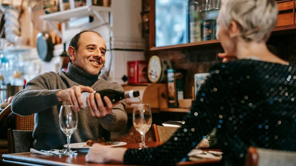 A man smiling while pouring wine for a woman at a cozy restaurant.
