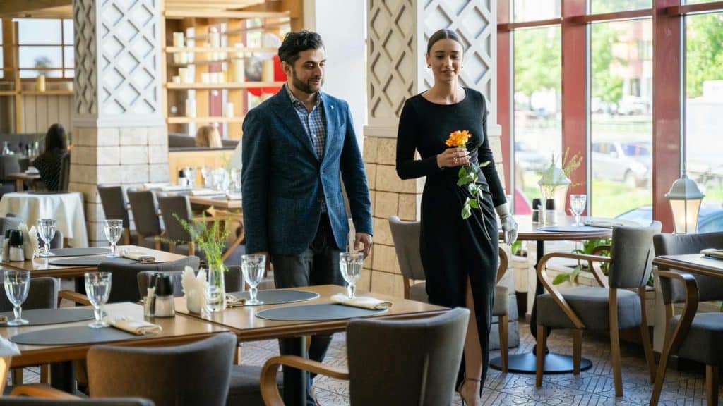 A man and a woman are walking into a restaurant, with the woman holding a flower.