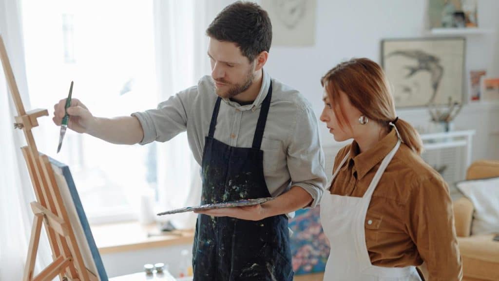 A man painting on a canvas while a woman watches beside him.