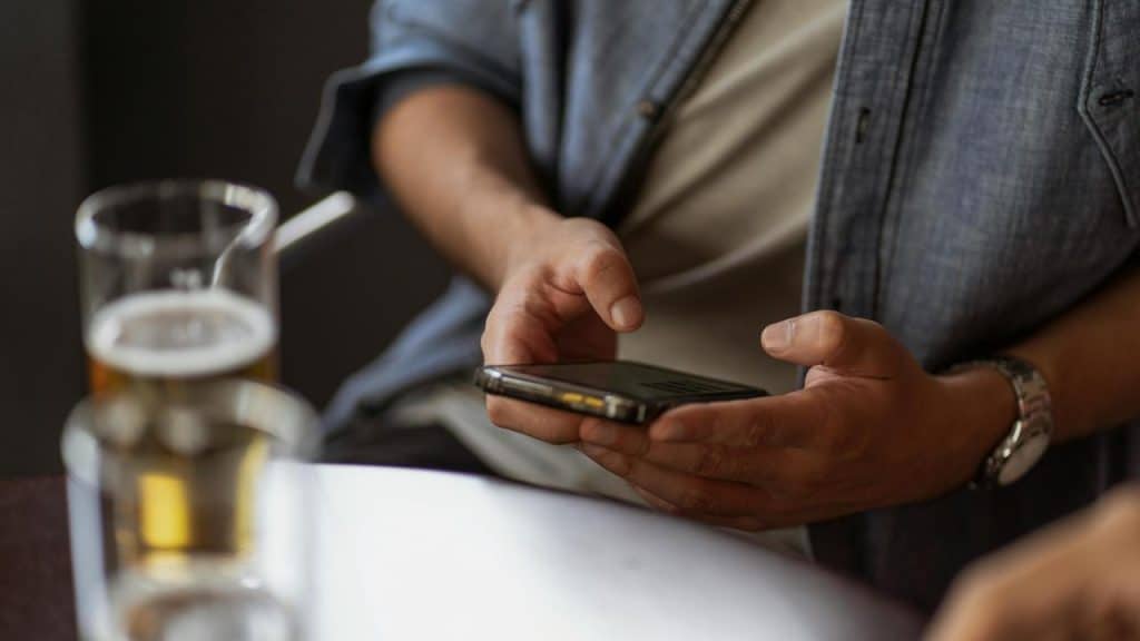 A man holding a smartphone at a table with drinks.
